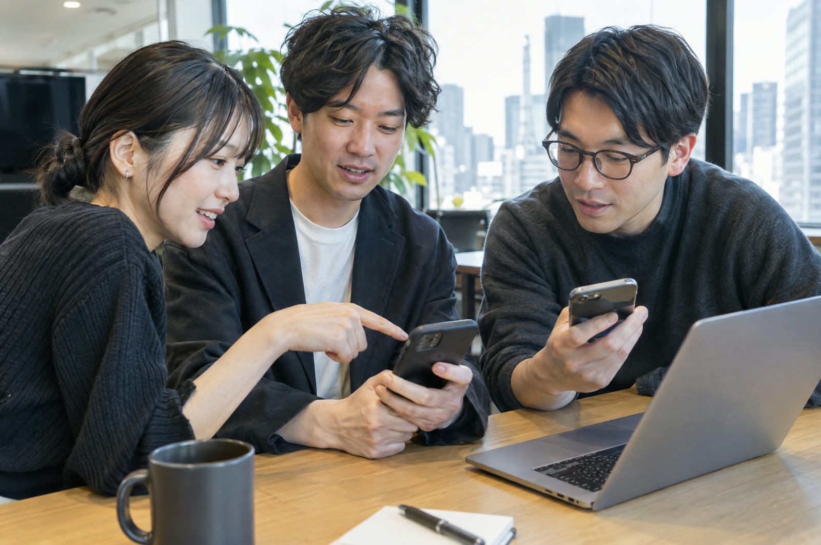 オフィスで三人のチームがスマートフォンとノートパソコンで縦動画を確認している